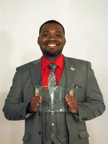 A photo of Aaron McCormick, smiling and wearing a red shirt, gray patterned tie and gray vest and blazer.